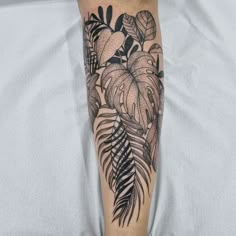 a black and white tattoo on the leg of a woman's legs with leaves