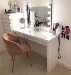 a white desk topped with a mirror and a pink chair next to an illuminated vanity