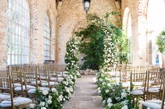 an indoor wedding ceremony with white flowers and greenery on the aisle, surrounded by chairs