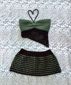 two crocheted swimsuits are laying on a white sheet and one has a green bow tie