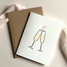 two cards with champagne glasses on them sitting next to each other in front of a piece of paper