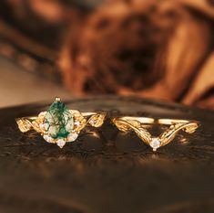 two gold rings with green and white stones sitting on top of a brown leather surface