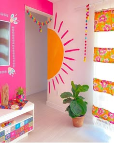 a living room with pink walls and colorful decorations on the wall, potted plant in front of window