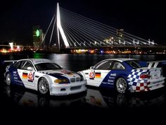 two racing cars parked next to each other in front of a bridge and water at night