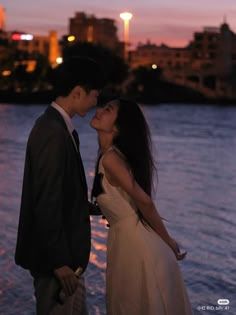 a man and woman standing next to each other in front of the water at sunset