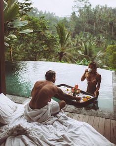 two people sitting on a bed in front of a swimming pool with food and drinks