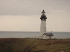 a light house sitting on top of a hill next to the ocean with an overcast sky