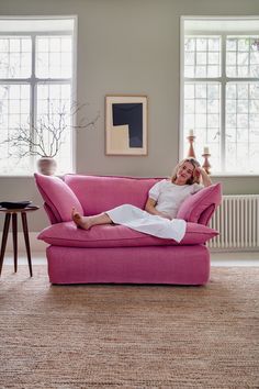 a woman laying on top of a pink couch in a living room next to two windows