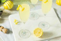 three glasses filled with lemonade sitting on top of a cutting board next to sliced lemons