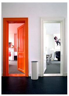 an orange door is in the middle of a room with white walls and black floors