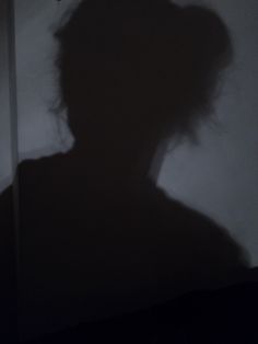 the shadow of a person holding an umbrella in front of a dark room with white walls