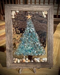 a christmas tree made out of seashells is displayed in a frame on a table