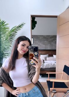 a woman taking a selfie with her cell phone in front of a bed room