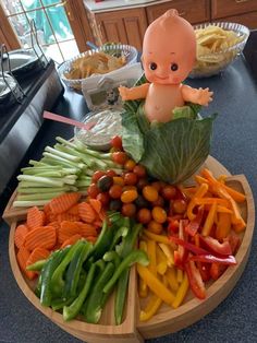 a baby doll sitting on top of a wooden plate filled with lots of veggies