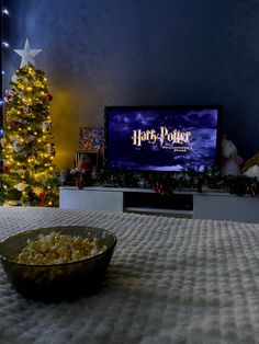 a bowl of popcorn sitting in front of a christmas tree with a harry potter movie on the screen