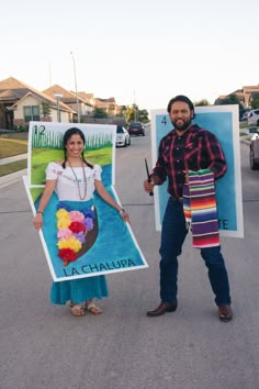 a man and woman standing in the middle of a street holding up large posters that say la chalupa