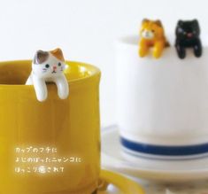 two small cats sitting on top of a yellow cup next to another cat figurine