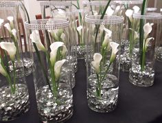 several clear vases filled with white flowers on a black table cloth covered tablecloth