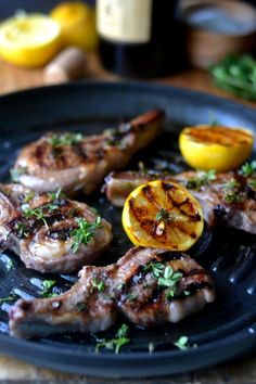 grilled meat with lemons and herbs on a black plate next to a bottle of wine