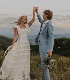 a man and woman in wedding attire holding hands while standing on top of a hill