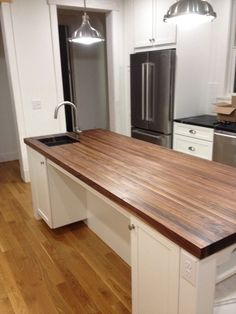 a kitchen with an island made out of wood and stainless steel appliances in the background