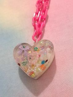 This is a handmade epoxy resin necklace with a plastic 50cm chain in iridescent pink. The charm is approximately 3.5 cm wide. This is an adorable necklace that would fit with a range of outfits and styles. It features many small pastel charms and lots of holographic glitter to catch the eye! The backing is holographic lilac. Each item is one of a kind and handmade - so each one is completely unique and special! Pink Heart Pendant Charm Necklace With Lobster Clasp, Pink Heart Charm Necklace For Party, Pink Heart-shaped Charm Necklace For Party, Pink Heart Charm Necklaces For Jewelry Making, Pink Heart-shaped Charm Necklaces With Lobster Clasp, Pink Heart-shaped Charm Necklace With Lobster Clasp, Cute Pink Resin Necklace, Resin Heart Charm Pendant Jewelry, Pink Heart-shaped Resin Jewelry