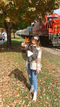 a woman standing in front of a train holding an orange leaf with her right hand