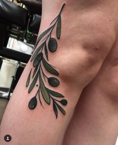 an olive branch tattoo on the right side of the leg, with black olives and green leaves