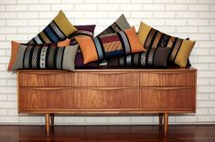 a bunch of pillows sitting on top of a wooden dresser next to a brick wall