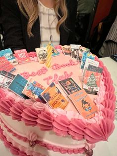 a woman sitting in front of a pink cake with books on it