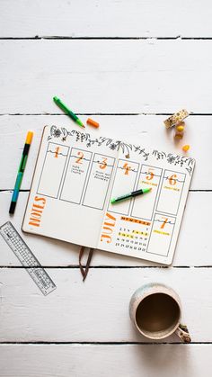 an open planner with pencils and markers next to a cup of coffee on a white wooden table