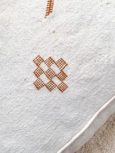 an embroidered piece of cloth with orange stitching on it sitting on top of a white towel