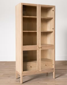 an oak bookcase with glass doors on the top and bottom shelves, in front of a white wall