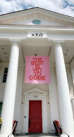 a pink sign that says the best is yet to come hanging on a white building