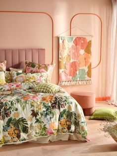 a bed with floral comforter and pillows in a pink room next to a window