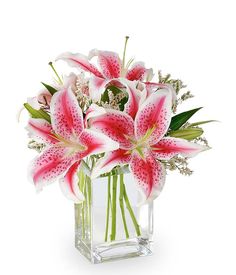 a vase filled with pink and white lilies on top of a table next to a window