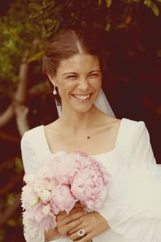 a woman in a wedding dress holding a bouquet of pink peonies and smiling at the camera