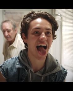 a young boy making a funny face while an older man looks on in the background