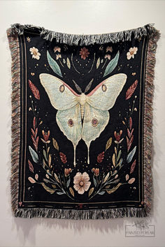 an embroidered wall hanging with a white butterfly on it's back and fringes around the edges