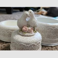 two white birds sitting on top of a vase with pink roses in the bottom,