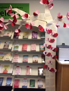 some pink and red paper hearts hanging from a book shelf next to a printer machine