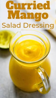 a glass jar filled with orange juice next to sliced limes on a table and text overlay that reads currie mango salad dressing