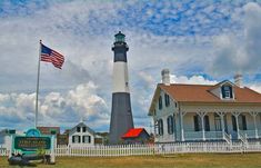 a lighthouse with an american flag flying in front of it and a white picket fence around it