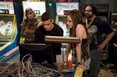 three people standing in front of a bunch of game machines with wires all over them