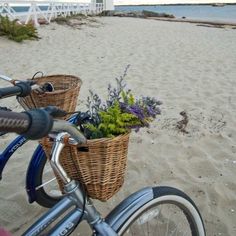 a bicycle parked on top of a beach next to a basket with flowers in it