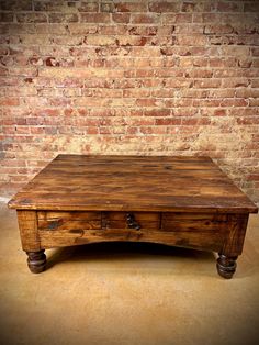 an old wooden coffee table in front of a brick wall with two drawers on each side