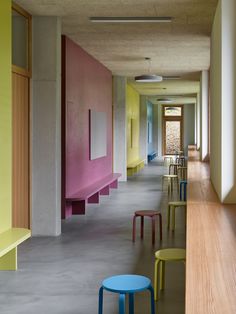 an empty hallway with several tables and chairs lined up against the wall in different colors