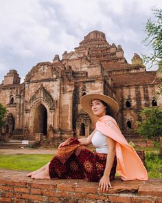 a woman wearing a hat and scarf sitting on a brick wall in front of an old building