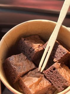 a person holding a bowl with brownies and chopsticks in it