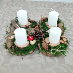 some white candles are sitting on top of moss and pinecones in the shape of a heart